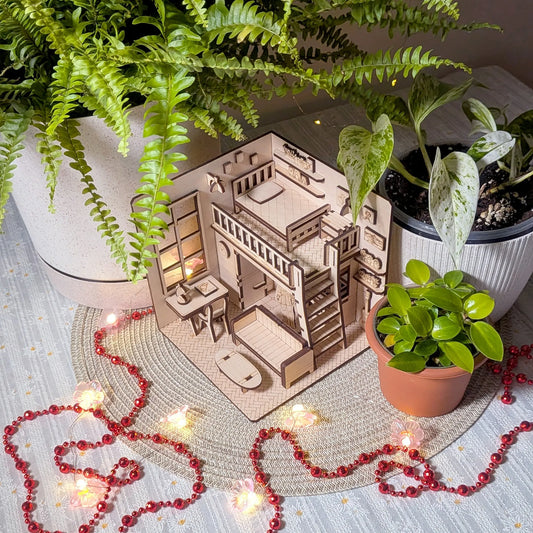 Miniature wooden house model with furniture surrounded by potted plants on a textured surface.