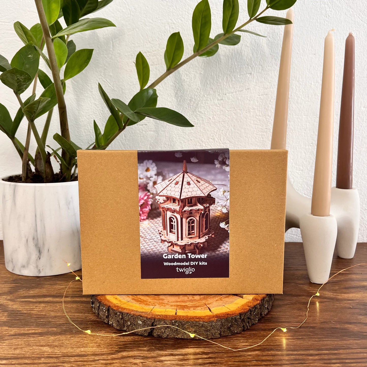 Wooden DIY kit packaging with garden tower design on a wooden surface with plants and candles in the background.