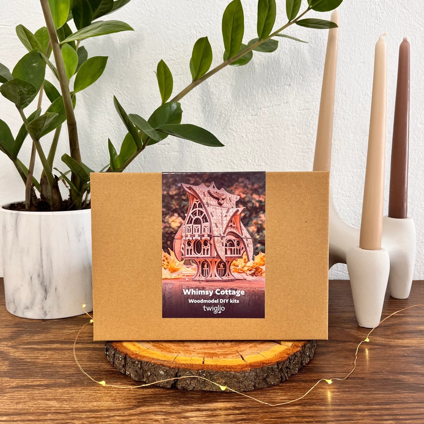 DIY kit packaging of garden cottage on a wooden surface with plants and candles in the background.