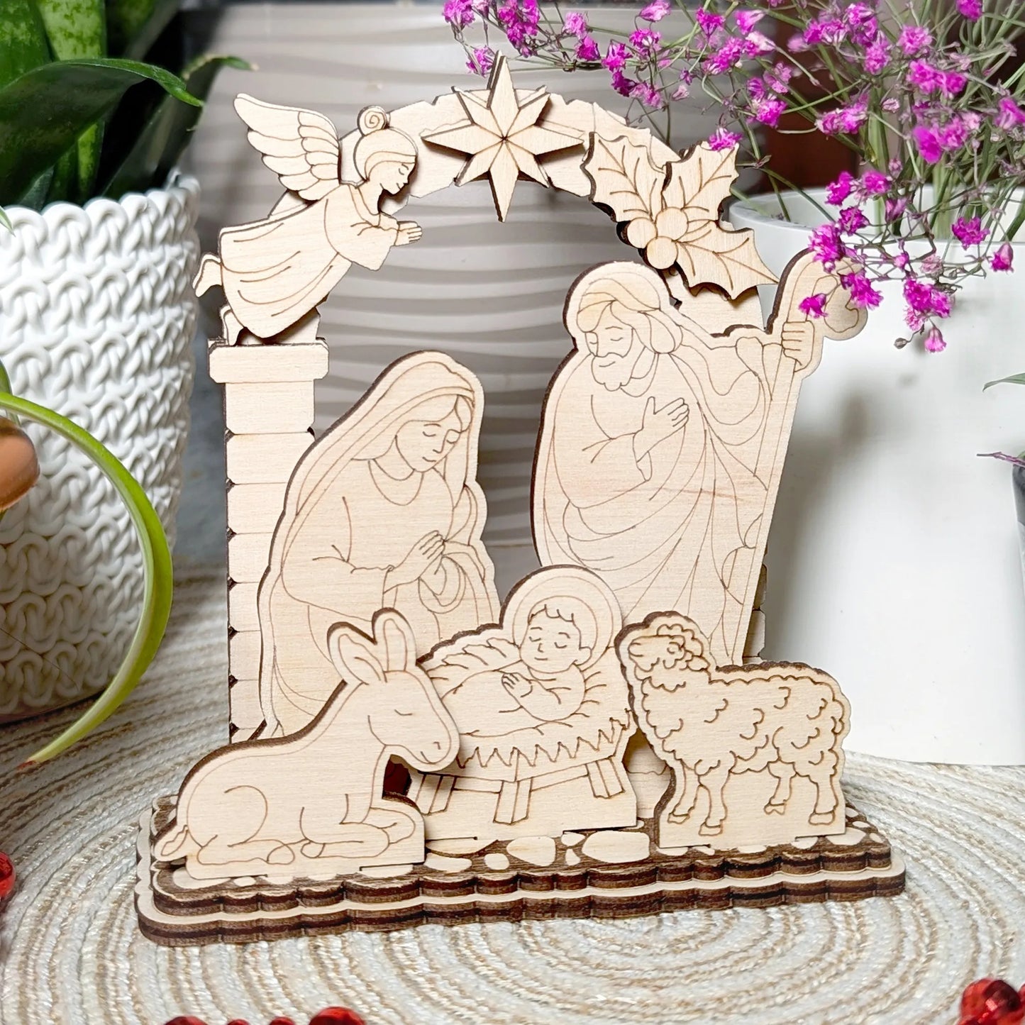 Wooden nativity scene with Mary, Joseph, baby Jesus, and animals on a textured surface with flowers in the background.
