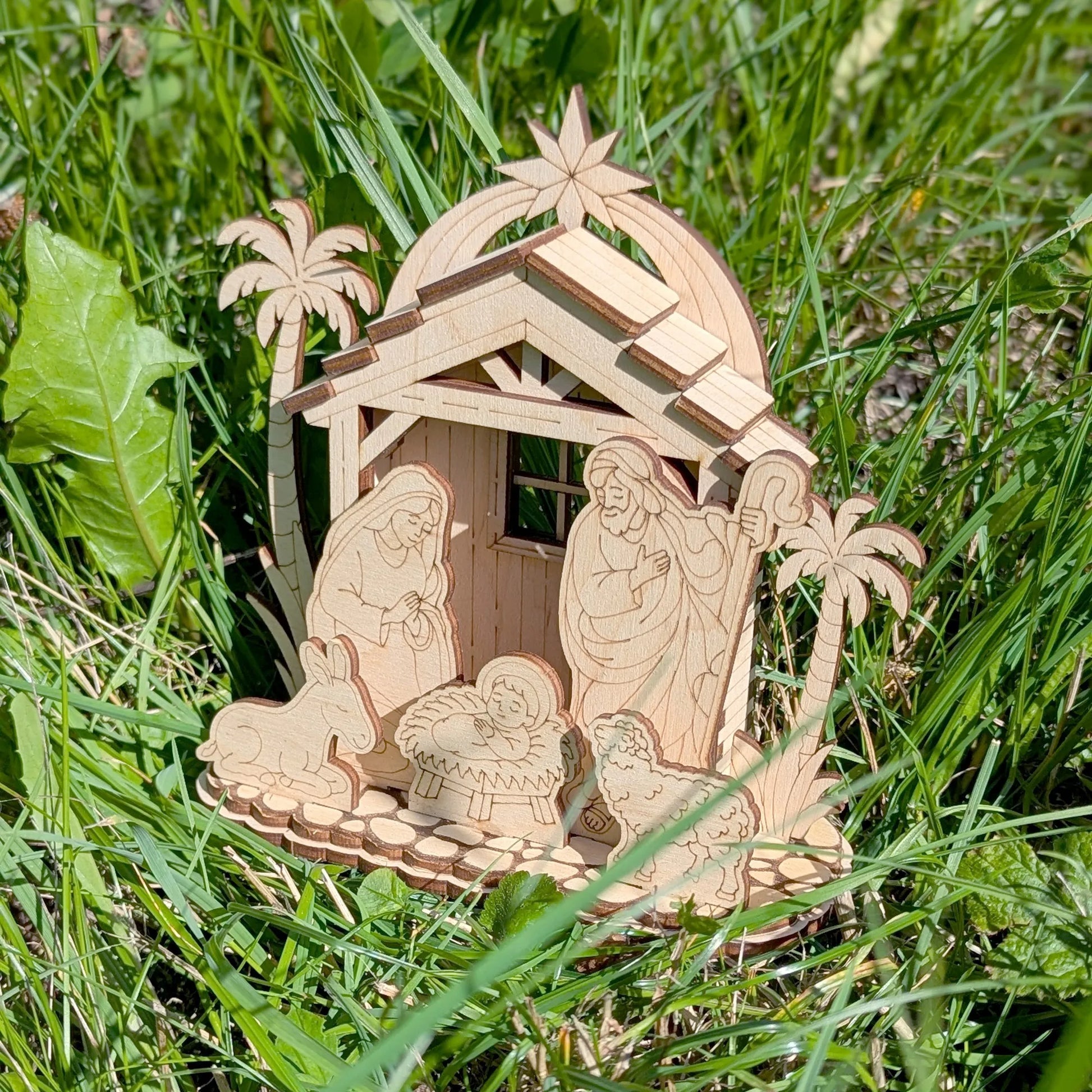 Wooden nativity scene with Mary, Joseph, and baby Jesus in a manger on grass.