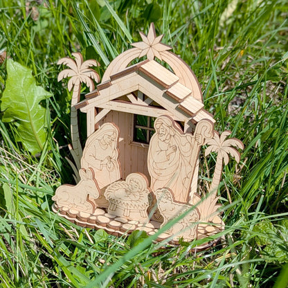Wooden nativity scene with Mary, Joseph, and baby Jesus in a manger on grass.