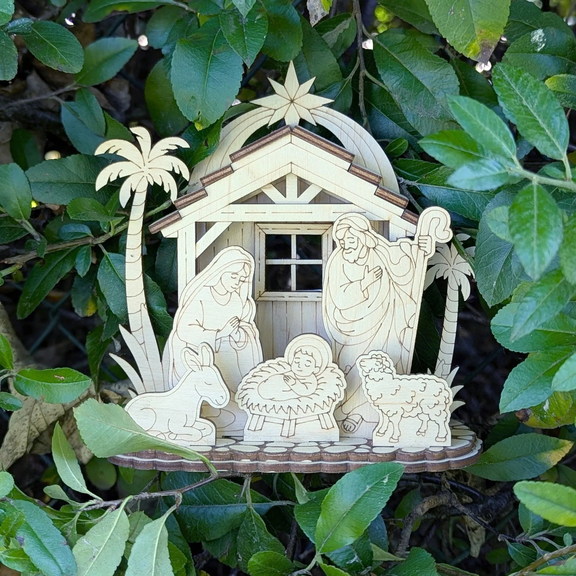 Decorative nativity scene with Mary, Joseph, and baby Jesus in a manger, surrounded by green leaves.