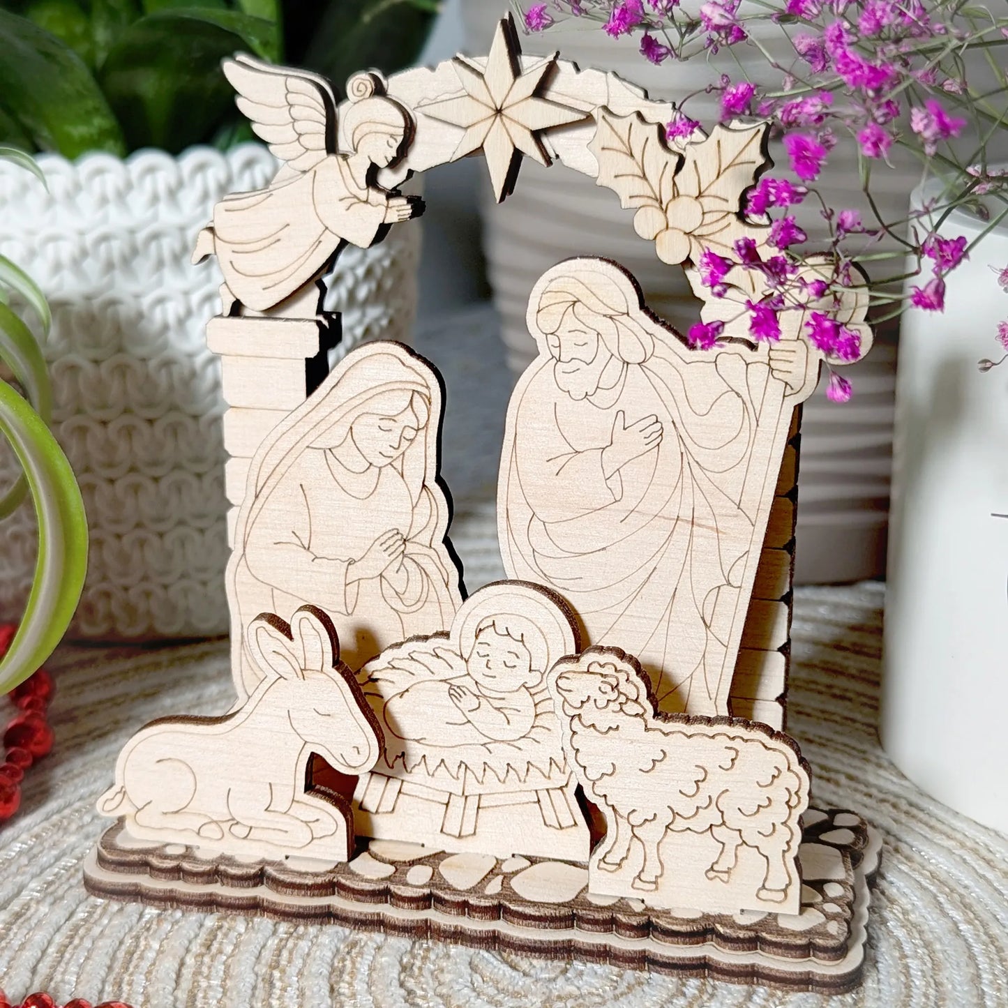 Wooden nativity scene with Mary, Joseph, baby Jesus, donkey, and sheep on a textured surface with flowers in the background.