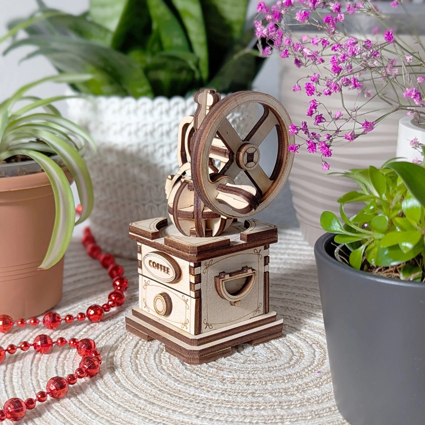 Wooden coffee grinder on a table with plants and beads in the background