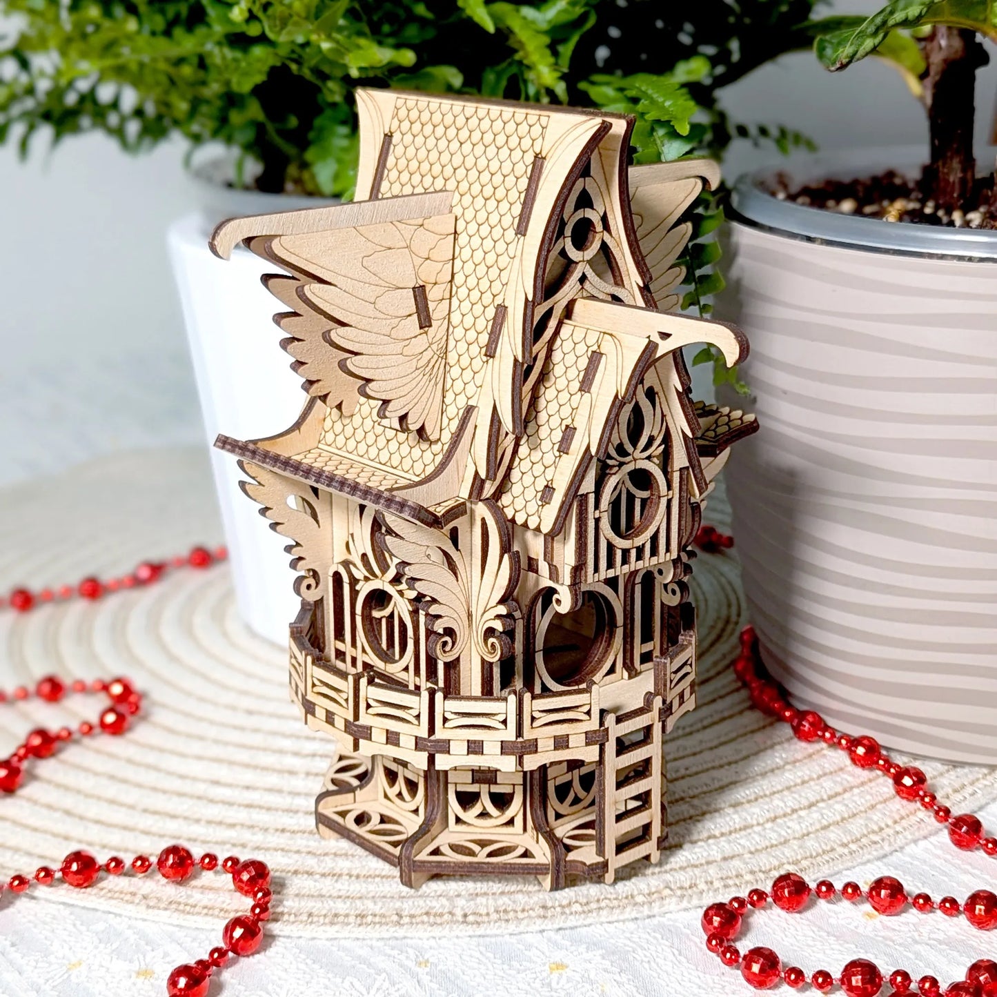 Wooden birdhouse model on a surface with red beads and plants in the background