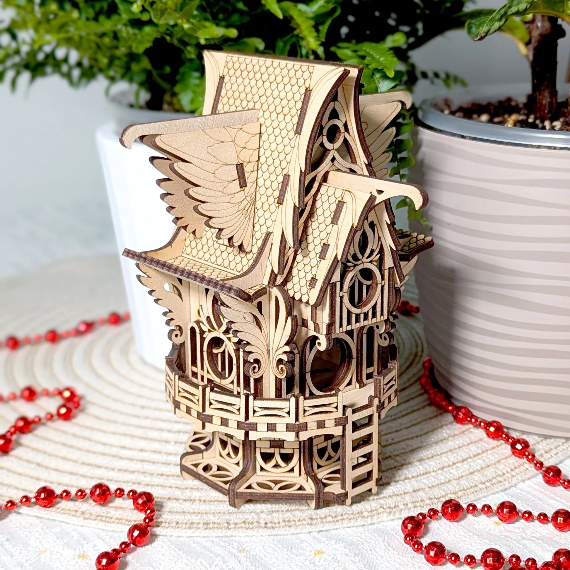 Wooden birdhouse model on a surface with red beads and plants in the background