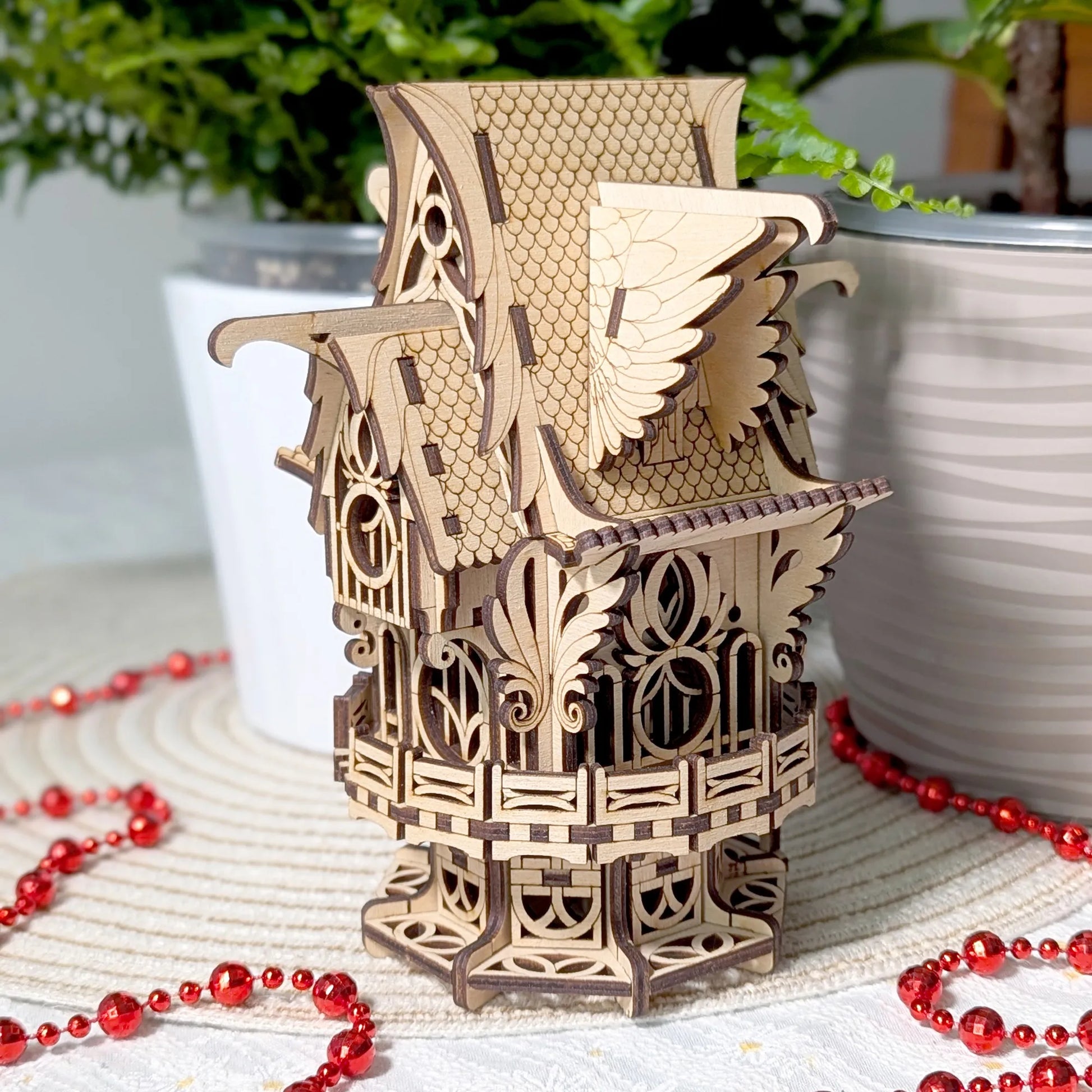 Wooden birdhouse model with red beads and plants in the background