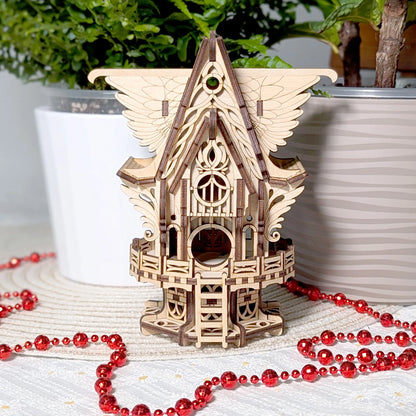 Wooden birdhouse model on a surface with red beads and plants in the background
