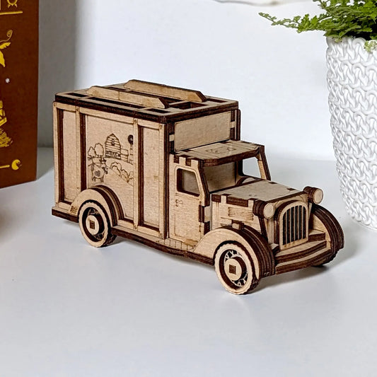 Wooden model of a vintage truck on a white surface with a plant in the background