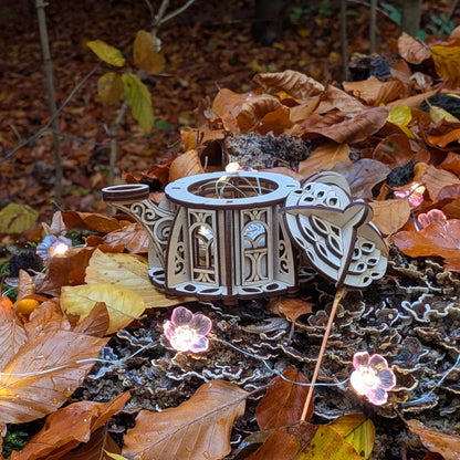 Decorative teapot with floral lights on a forest floor with fallen leaves
