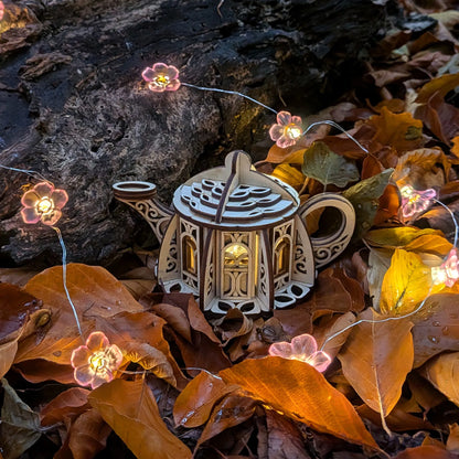 Decorative teapot with string lights on autumn leaves