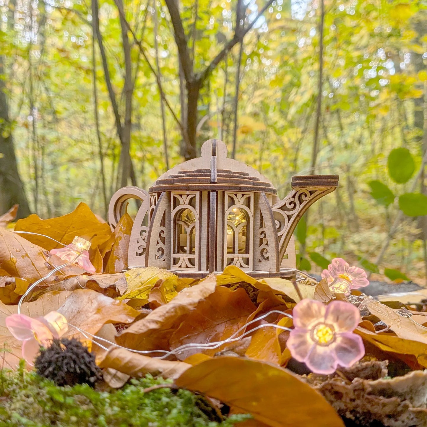handmade style wooden teapot house with fairy lights on autumn leaves in a forest setting