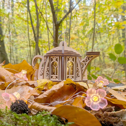 handmade style wooden teapot house with fairy lights on autumn leaves in a forest setting