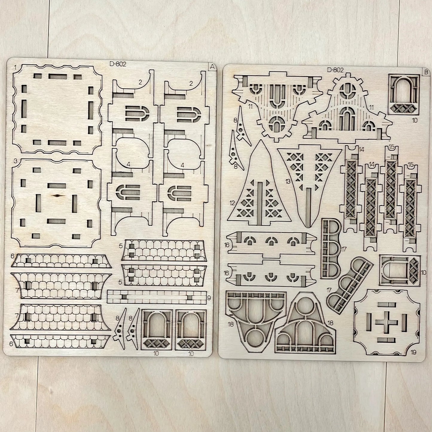 Two wooden model building kits with architectural designs on a light wooden surface.
