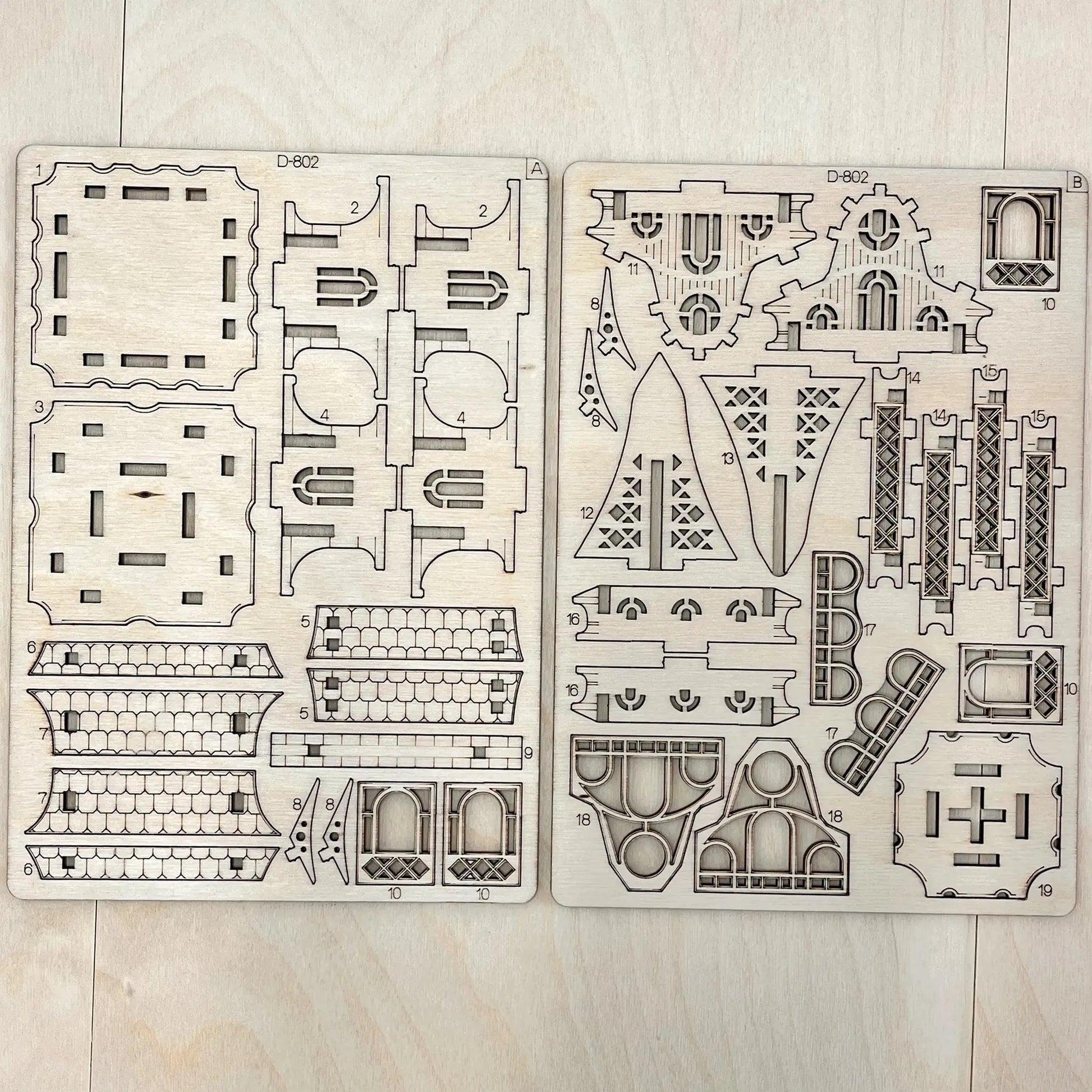 Two wooden model building kits with architectural designs on a light wooden surface.