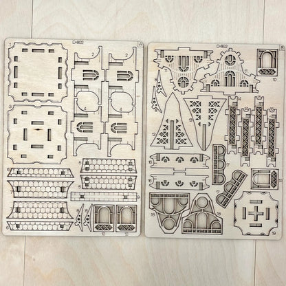 Two wooden model building kits with architectural designs on a light wooden surface.