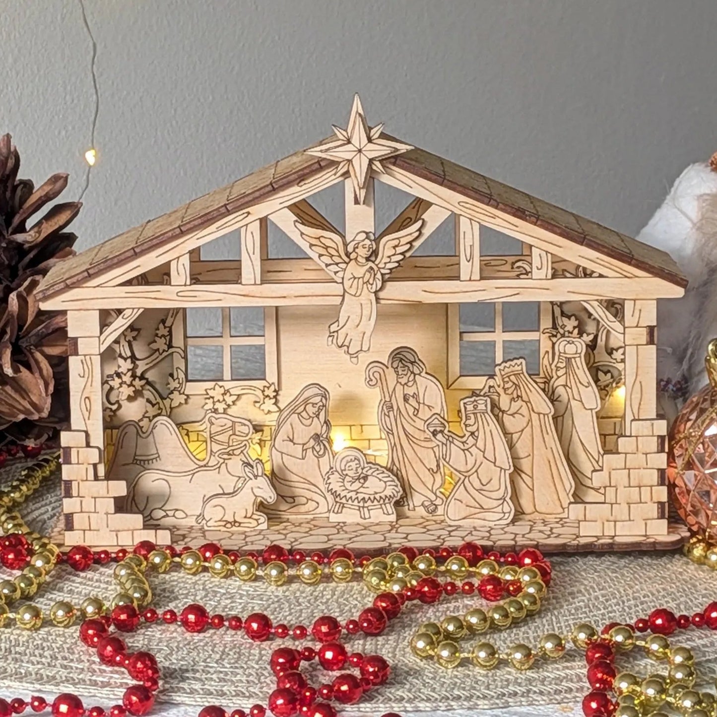Wooden nativity scene with figurines and a star on top, surrounded by Christmas decorations.