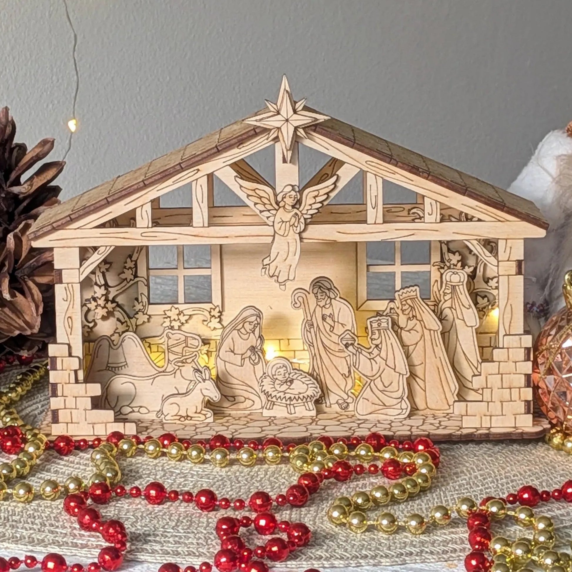 Wooden nativity scene with figurines and a star on top, surrounded by Christmas decorations.