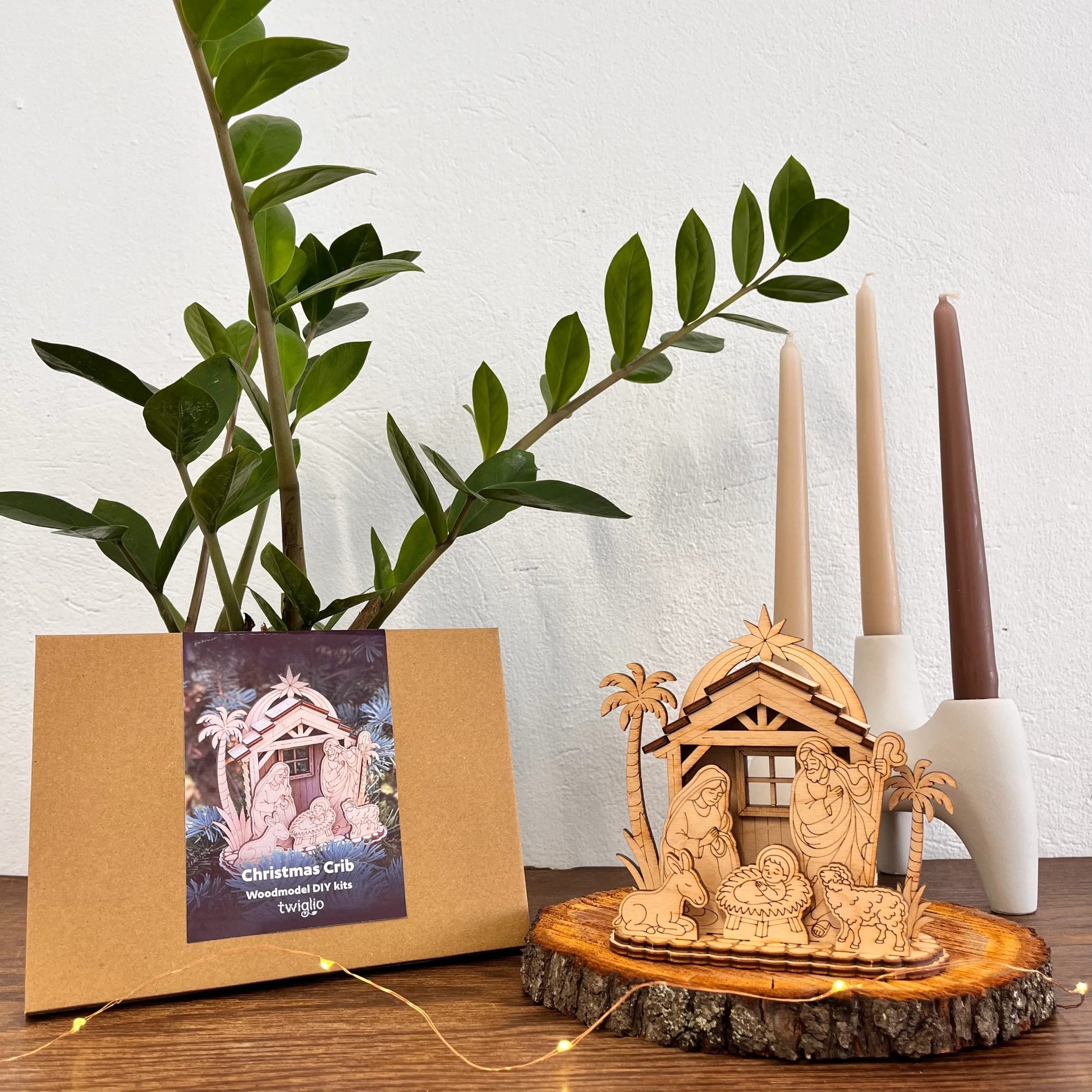 Wooden nativity scene on a wooden base with a cardboard box and candles in the background.