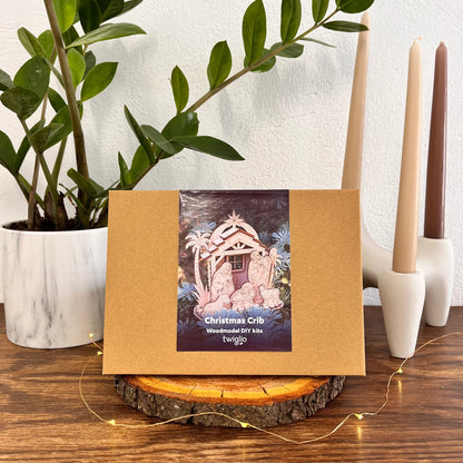 Cardboard box with Christmas crib design on a wooden surface with candles and a plant.