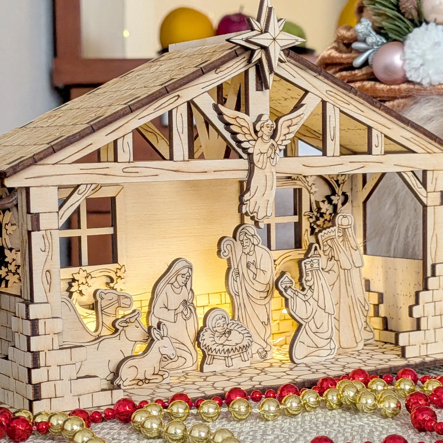 Wooden nativity scene model with illuminated interior, surrounded by Christmas decorations.
