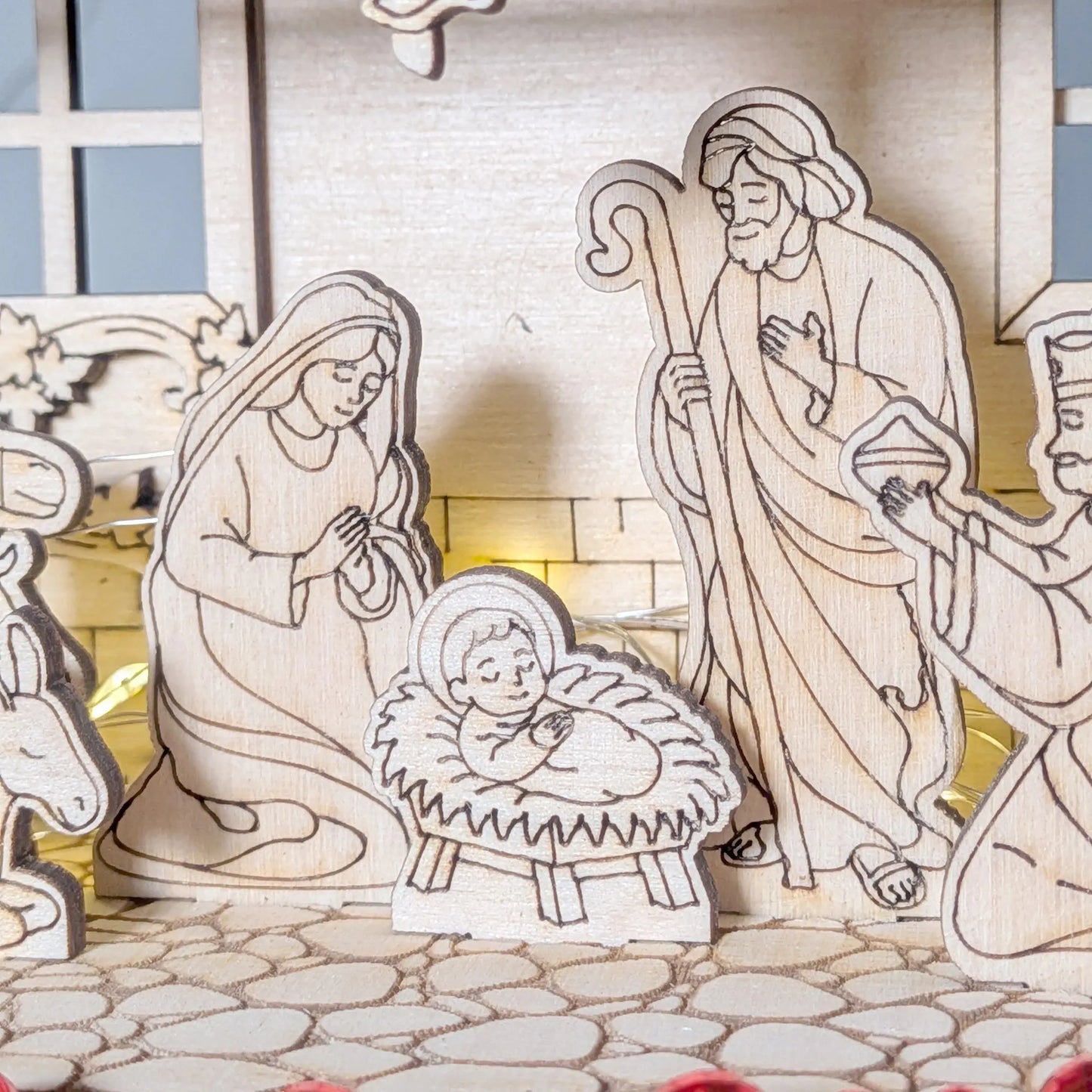 Wooden nativity scene with Mary, Joseph, and baby Jesus on a stone path.