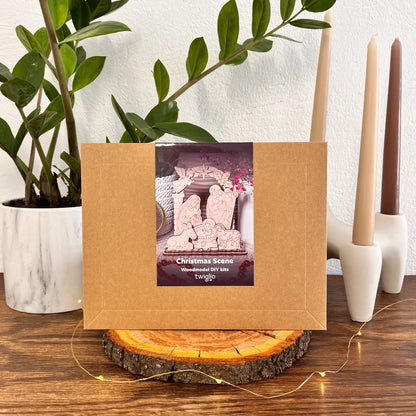 Wooden frame with a Christmas scene woodmodel DIY kit on a wooden surface with candles and a plant in the background.