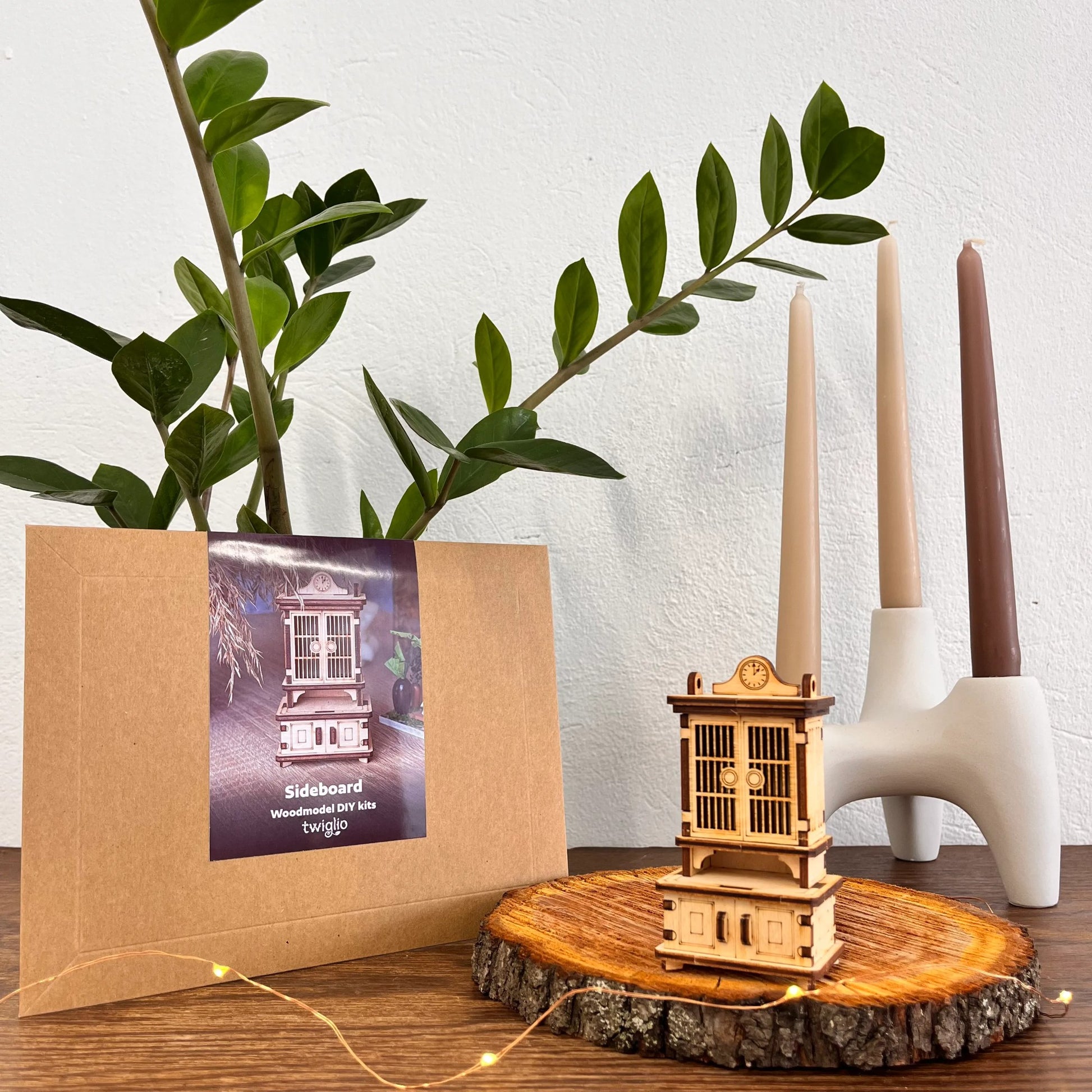 Wooden model of a sideboard on a wooden slice with a plant and candles in the background.