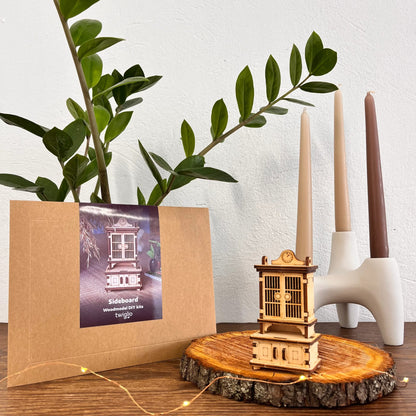 Wooden model of a sideboard on a wooden slice with a plant and candles in the background.