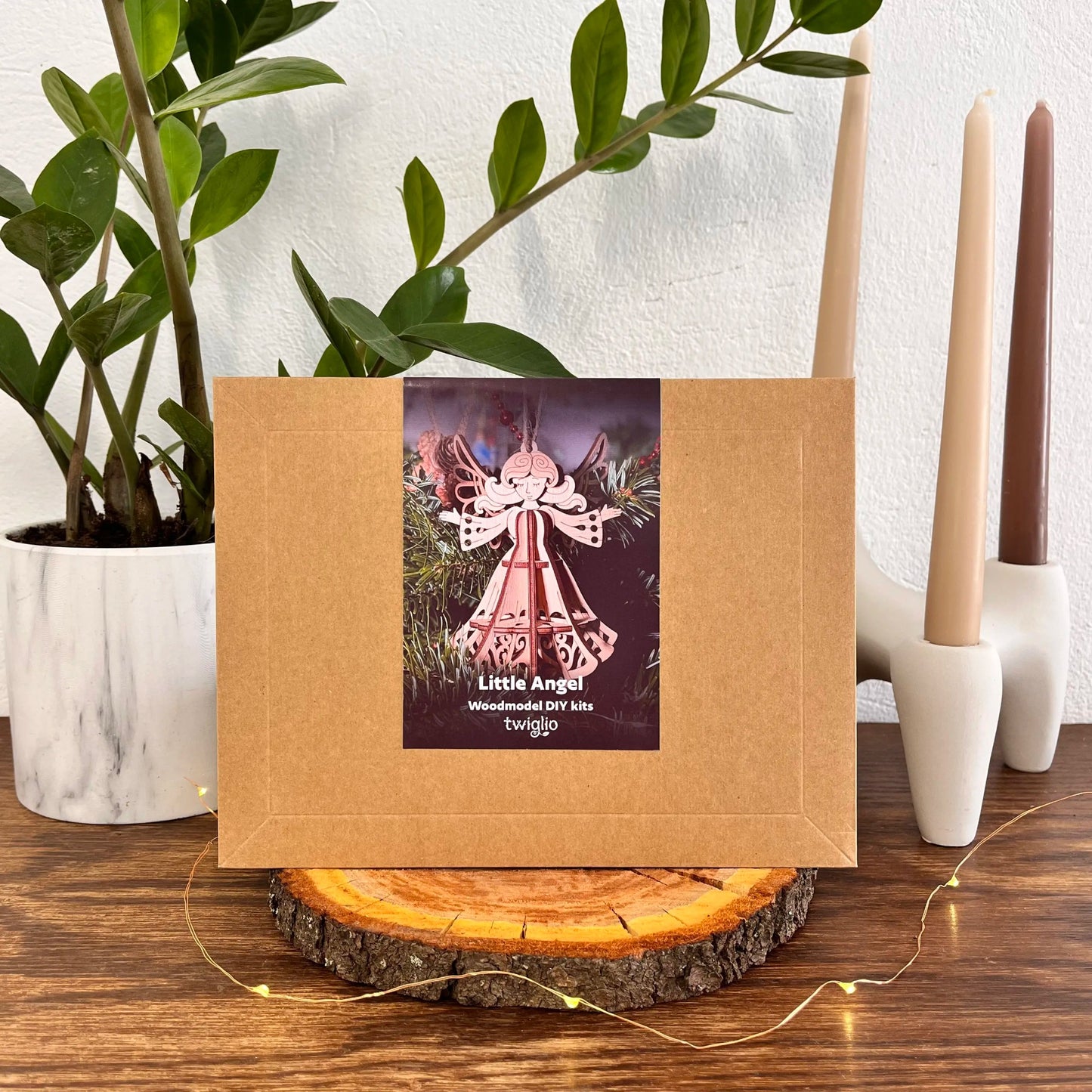 Wooden model kit packaging with 'Little Angel' label on a wooden surface with plants and candles in the background.