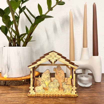 Wooden nativity scene with candles on a wooden surface with a plant and candle holder in the background.