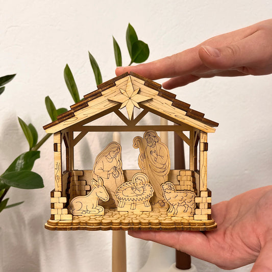 Wooden nativity scene model held by a hand with a plant in the background
