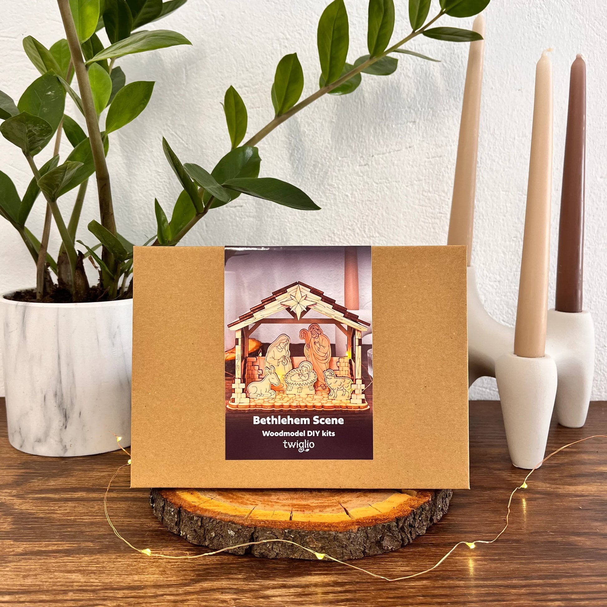 Brown box with Bethlehem Scene wooden DIY kit on a wooden surface with candles and a plant in the background.