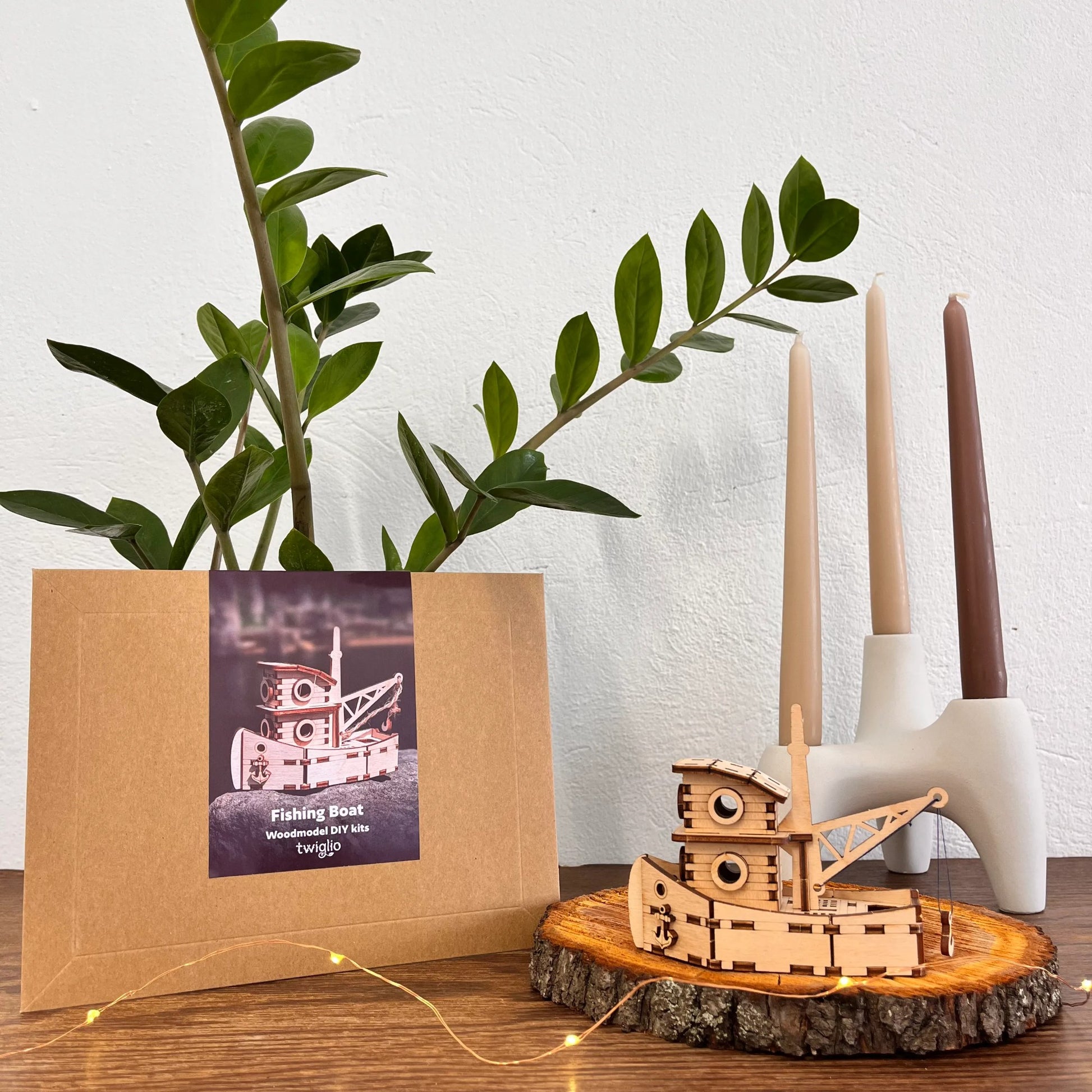 Wooden model boat ship on a wooden stand with a plant and candle holder in the background.