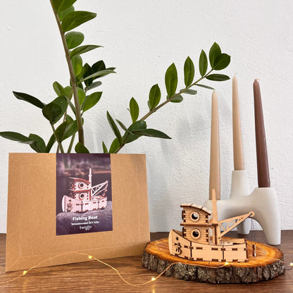 Wooden model boat ship on a wooden stand with a plant and candle holder in the background.