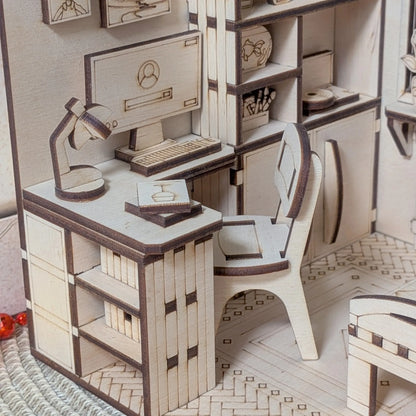 Wooden model of a room with a desk, chair, and computer setup.