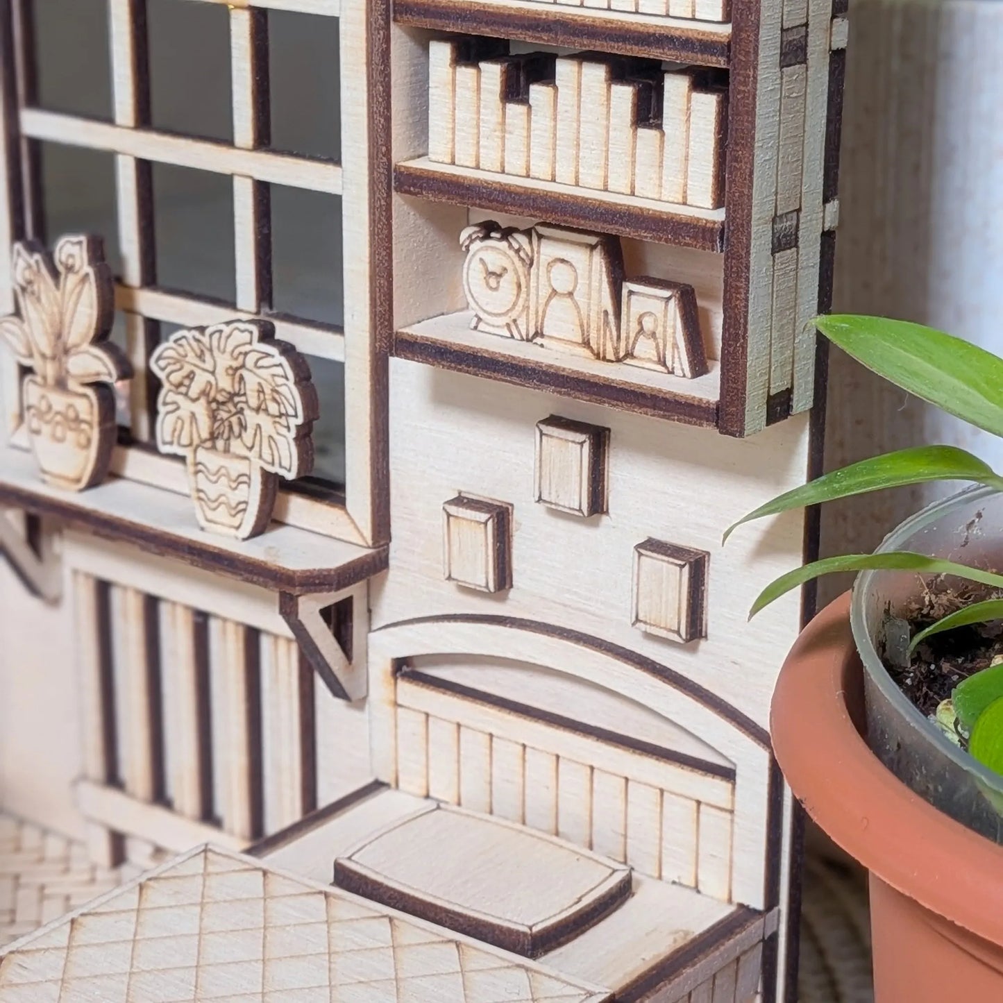 Close-up of a miniature model of a room with shelves and decor, next to a potted plant.