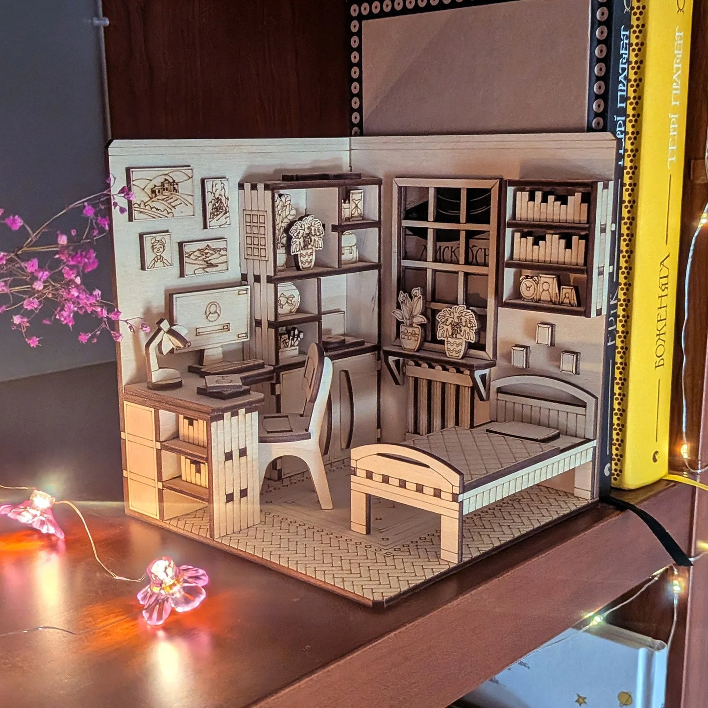 Wooden model of a room with furniture and decor, illuminated by small lights.
