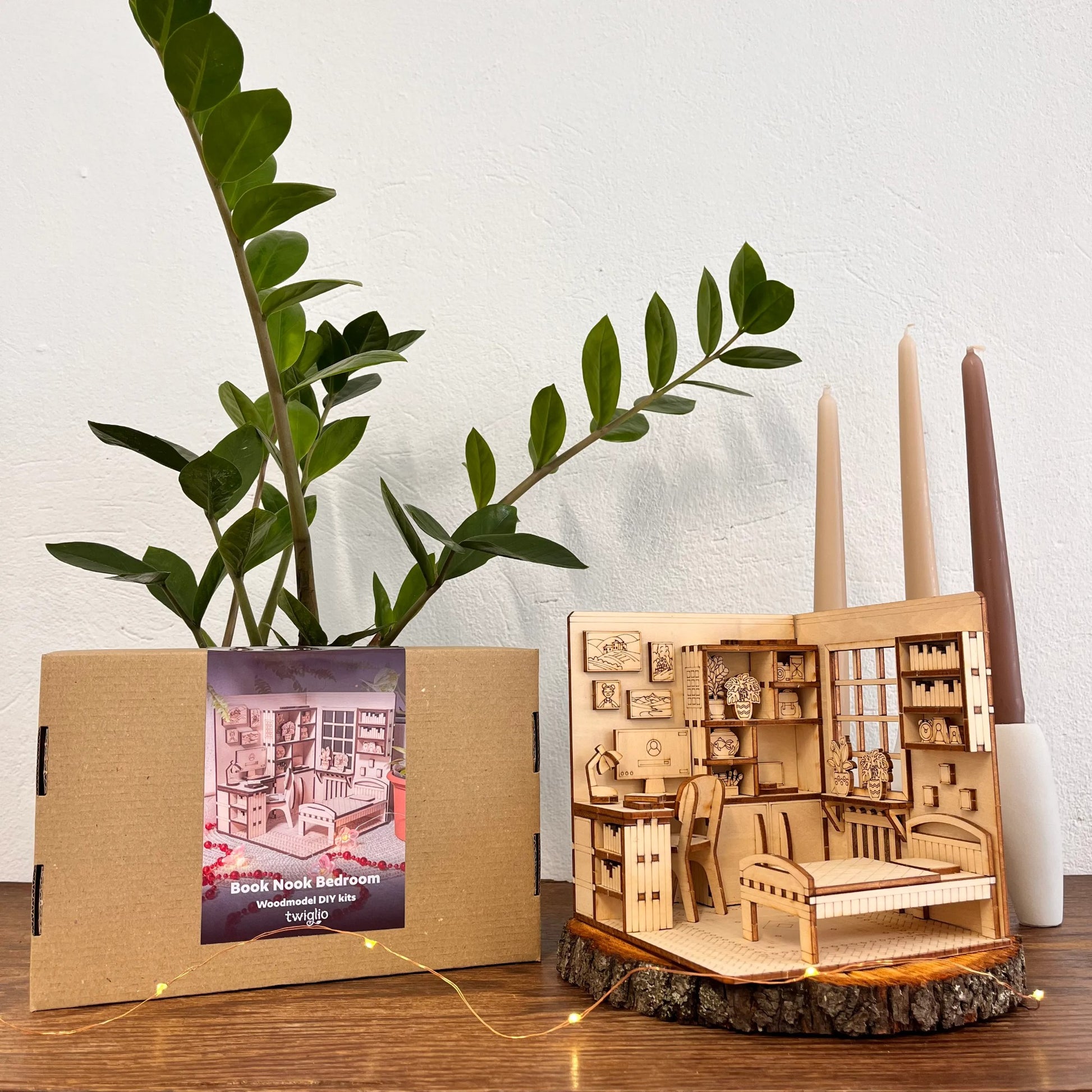 Wooden model of a room with furniture, candles, and a plant on a wooden surface.