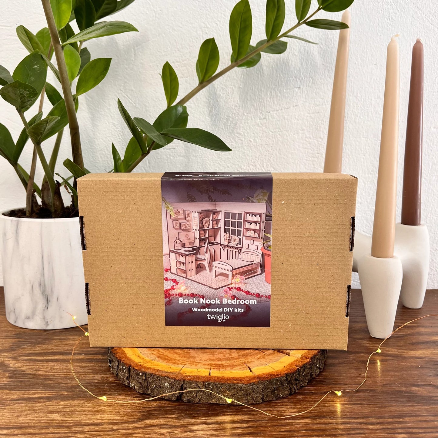 Wooden model kit packaging on a wooden stand with candles and plants in the background