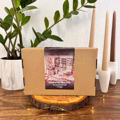 Wooden model kit packaging on a wooden stand with candles and plants in the background