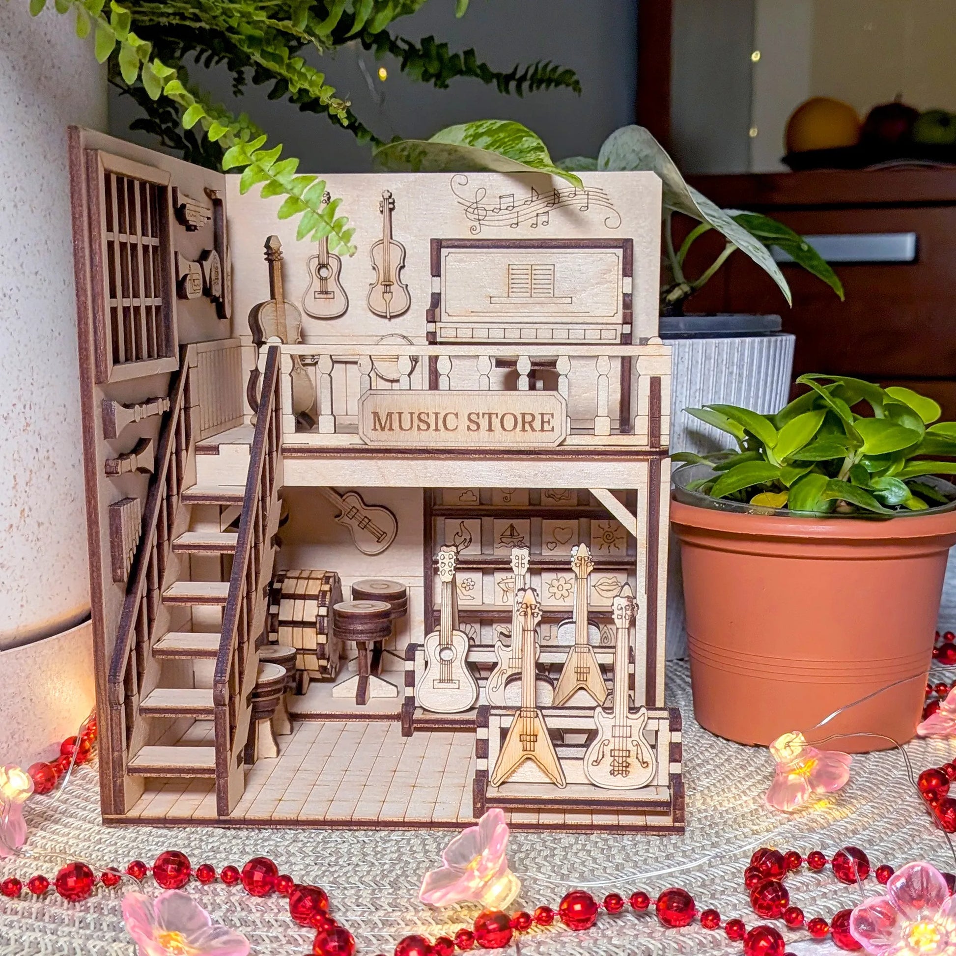 Wooden model of a music store with guitars and furniture, surrounded by plants and decorative items.