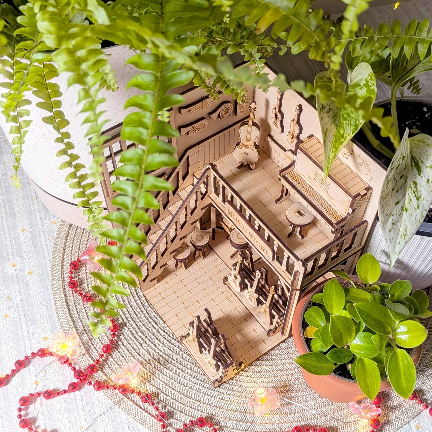 Wooden model of a house with people on a table surrounded by plants