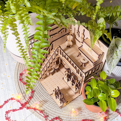 Wooden model of a house with people on a table surrounded by plants