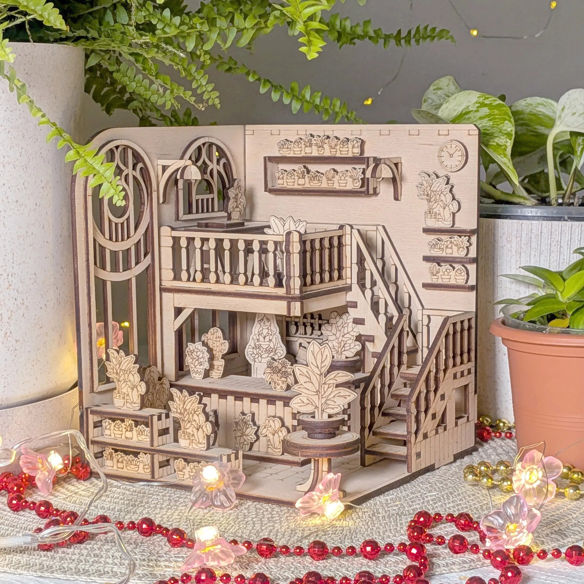 Wooden book nook model with intricate details on a decorative surface with plants and lights.