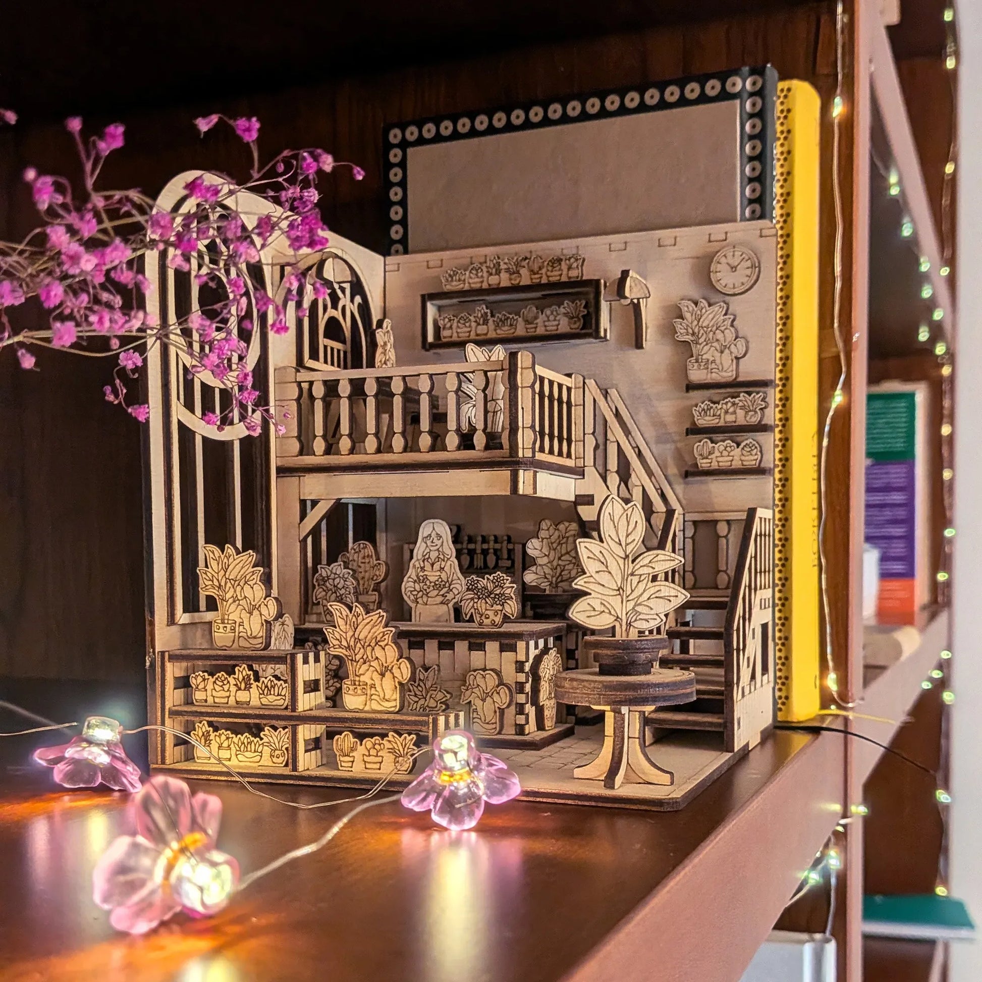 Wooden book nook model with detailed furniture and decor on a wooden surface.