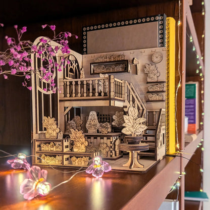 Wooden book nook model with detailed furniture and decor on a wooden surface.