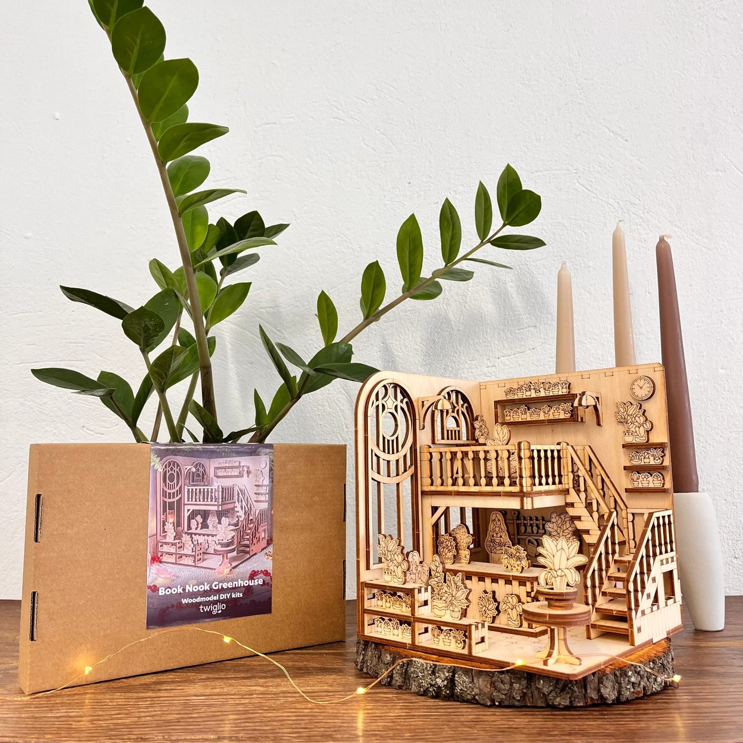 Wooden model book nook green house on a wooden stand with a plant and candle holder in the background.