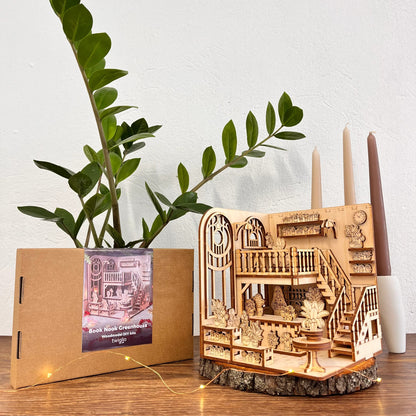 Wooden model book nook green house on a wooden stand with a plant and candle holder in the background.